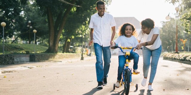Two parents helping their young daughter learn to ride a bike